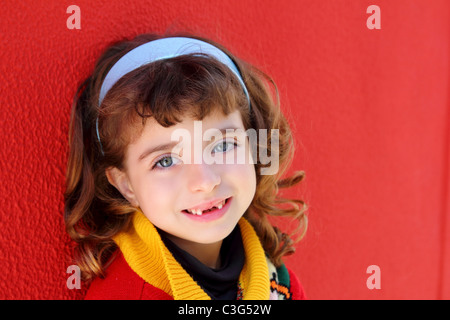 Sorridente bambina frastagliate denti frontali sorriso sul muro rosso sfondo Foto Stock