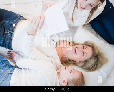 La madre e le figlie (8-11) lettura la lettera sul letto Foto Stock
