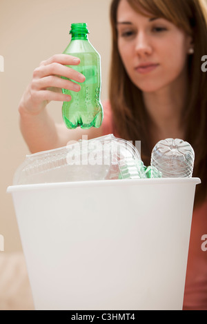 Studio shot di donna (8-9) collocando la bottiglia di plastica nel contenitore di riciclaggio Foto Stock