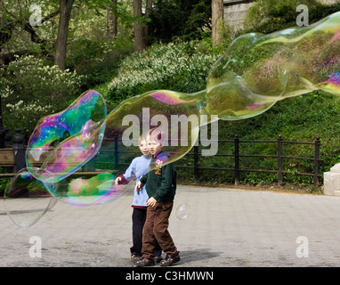 Due giovani ragazzi fissando in stupore di fronte a enormi bolle di sapone nel Central Park di New York City. Foto Stock