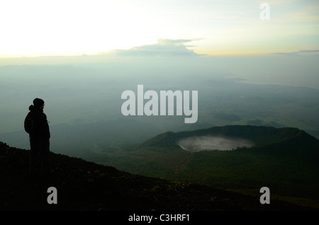 Escursionista guardando in giù sul piccolo cratere e il lago Kivu dalla parte superiore del Nyiragongo vulcano attivo nel Parco nazionale di Virunga, nella Repubblica democratica del Congo. Foto Stock