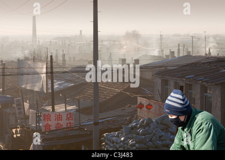 Le emissioni da carbone home incendi in Suihue,Cina con un ciclista che indossa una maschera di smog. Foto Stock