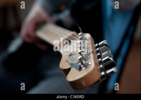 Un dettaglio di una chitarra in una mano di un giovane maschio adulto pensando di giocare nel suo studio di casa. Foto Stock
