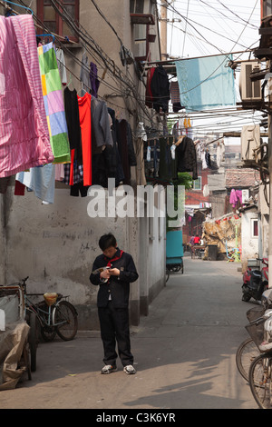 Ragazzo che guarda al telefono cellulare in vicoli di Shanghai, Cina Foto Stock