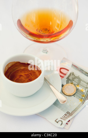 Bicchiere di cognac e caffè con monete e banconote in euro Foto Stock