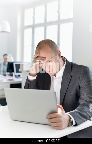Uomo seduto in ufficio guardando il computer portatile Foto Stock