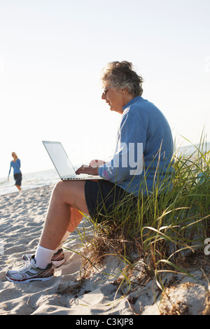 Senior donna utilizzando laptop sulla spiaggia Foto Stock