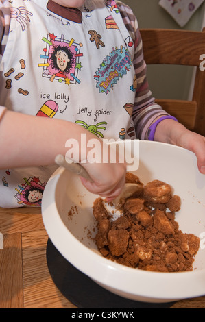 Torta di cottura della ragazza giovane, mescolando gli ingredienti (burro & zucchero di canna) in ciotola con il cucchiaio di legno & che indossa il grembiule del Beaker di Tracy - Yorkshire, Inghilterra UK Foto Stock