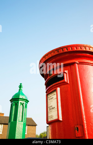 Un rosso brillante Postbox sorge accanto ad un verde brillante della pompa acqua in Thaxted, Essex. Foto Stock