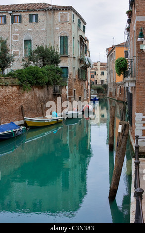 Una zona isolata e tranquilla di Venezia con le case e le barche si riflette nelle verdi acque del canale. Foto Stock