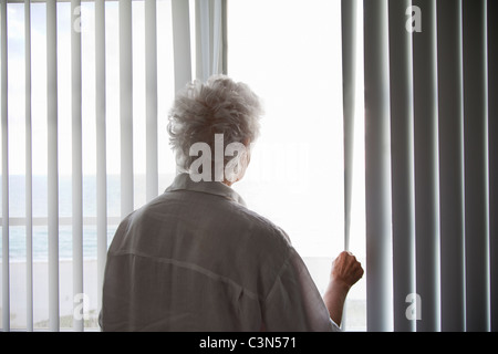 Senior Donna che guarda fuori da una finestra Foto Stock