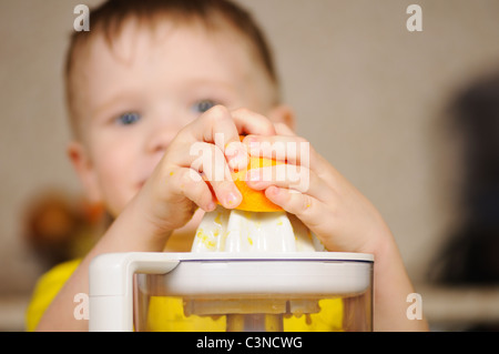 Il bambino in un giubbotto di colore giallo per strizzare fuori dal succo di un arancio Foto Stock