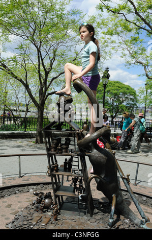 Una ragazza arroccato in cima a una scultura a Tom Otterness" "Il mondo reale" in Battery Park City sembra essere il padrone di ciò che ella sondaggi. Foto Stock