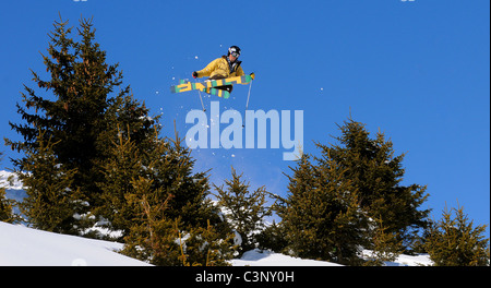 Uno sciatore vola attraverso l'aria dopo aver colpito un salto per cancellare gli alberi fuori pista francesi nella località sciistica di Courchevel nelle Alpi. Foto Stock