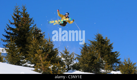 Uno sciatore vola attraverso l'aria dopo aver colpito un salto per cancellare gli alberi fuori pista francesi nella località sciistica di Courchevel nelle Alpi. Foto Stock