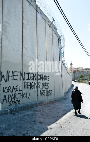 Una donna Palestinese passeggiate all'ombra della separazione israeliano parete divisoria zone palestinesi di Gerusalemme Est. Foto Stock