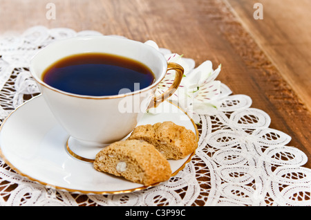 Cookie e caffè con fiore su sfondo di legno decorato con pizzo bianco igienico Foto Stock