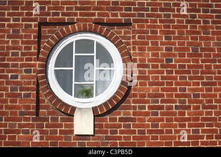 Finestra rotonda in rosso di un muro di mattoni. Foto Stock