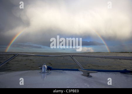 Rainbow formando come nuvole temporalesche chiaro come si vede da una piccola barca in mare Foto Stock