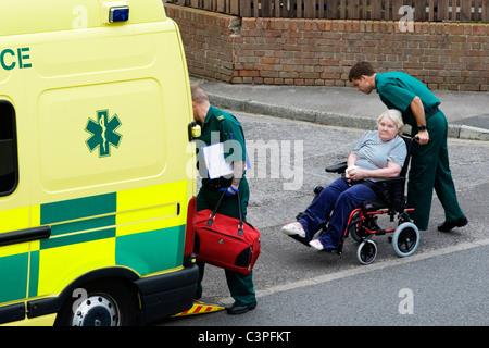 Signora anziana vittima di corsa essendo presa ad un ambulanza in una sedia a rotelle Foto Stock