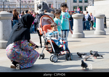 Londra , Westminster , Trafalgar Square , famiglia , madre in hijab & tre bambini piccoli , 1 in passeggino , alimentazione piccioni Foto Stock