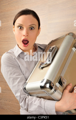 Ritratto di una giovane e bella imprenditrice tenendo una valigia e di essere rimasto sorpreso. Sfondo di Office. Foto Stock