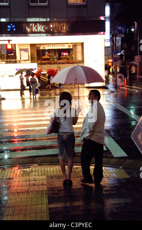 Coppia giapponese attendere per taxi sulla notte piovosa volta Tokyo street Foto Stock