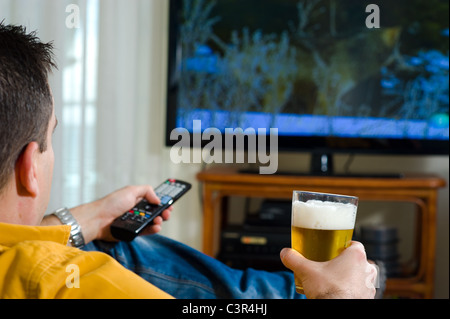 Guy godendo la sua sera birra davanti alla televisione Foto Stock