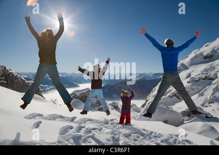 La famiglia felice salta in montagne invernali Foto Stock