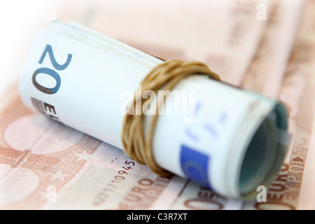 Arrotolato 20 banconote in una fascia elastica sul fuori fuoco 10 le banconote in euro Foto Stock