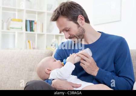 In Germania, in Baviera, Monaco di Baviera, padre alimentando il latte al bimbo (6-11 mesi) nel soggiorno Foto Stock