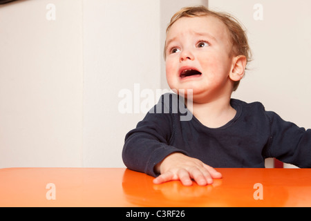 Piccolo Ragazzo seduto sulla tavola di piangere Foto Stock