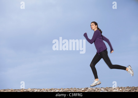 Donna jogging lungo la spiaggia ghiaiosa Foto Stock