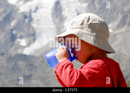 Un giovane ragazzo sat gustando un drink e un picnic al Kreuzboden nella valle di Saas, Svizzera. Foto Stock