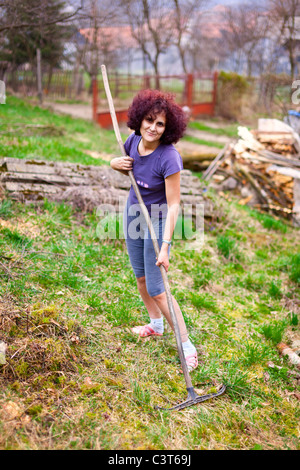 Giovani redhead lady utilizzando un rastrello per pulizia di primavera il suo giardino Foto Stock