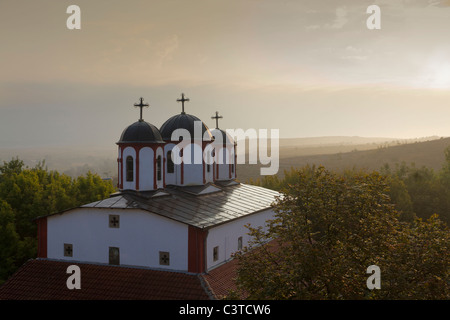 Struttura ad albero rosso a cupola chiesa bianca in golden mattina presto la luce in una nebbiosa scenari montuosi in Macedonia Foto Stock