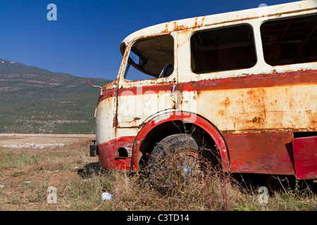 Stripped arrugginito, vecchio abbandonato bus rosso relitto in arido paesaggio montuoso del Montenegro Foto Stock