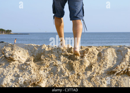 L uomo per le gambe sulla cima di una duna di sabbia, camminando verso il mare Foto Stock