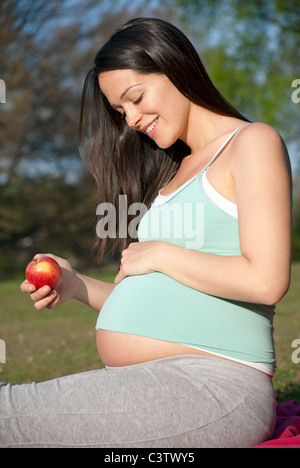 Un sano donna incinta azienda apple che guarda il suo crescente bump Foto Stock