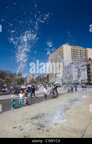 Una fontana progettata da bagnato getta acqua in aria di fronte al Brooklyn Museum di arte come i bambini guardare nella gioia. Foto Stock