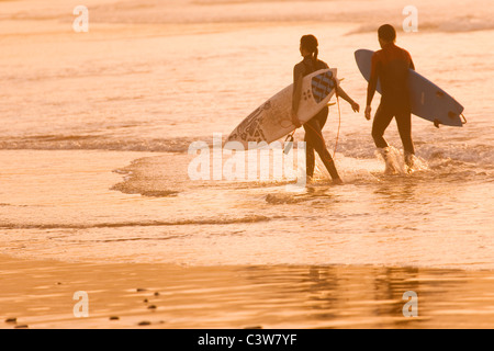 Due surfisti a piedi lungo in acqua poco profonda al tramonto Foto Stock