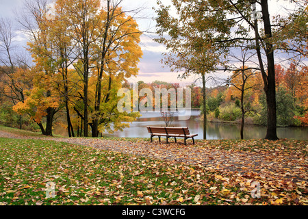 Un percorso a piedi e una panchina nel parco che si affaccia su di un lago in un giorno di pioggia in autunno, Sharon boschi, Southwestern Ohio, Stati Uniti d'America Foto Stock