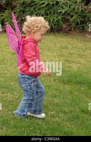 Bambino blondie ragazza con i capelli corti e costume butterfly wings camminare sull'erba. Foto Stock