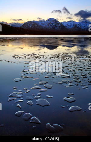 Snow-rivestiti montagne e acque ghiacciate di Lochan na h-Achlaise in Rannoch Moor, Scozia Foto Stock