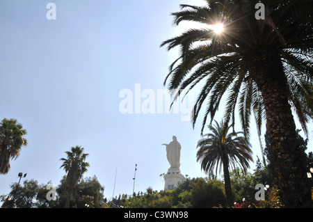 La statua della Vergine Maria, con il sole che splende attraverso un primo piano Palm tree, summit San Cristobal Hill, Santiago del Cile Foto Stock