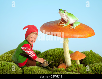 Ragazzo vestito come un giardino di gnome e una rana su un toadstool come in una favola Foto Stock