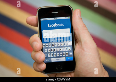 Stretta di mano di sesso maschile in possesso di un iPhone per accedere a Facebook. (Solo uso editoriale). Foto Stock