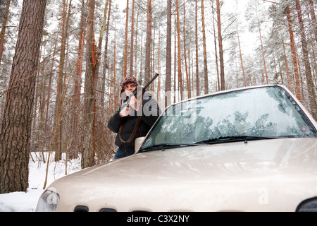 Uomo con il fucile da cecchino e jeep nella foresta d'inverno. Ampio angolo di ripresa. Foto Stock