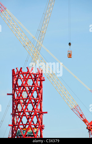 Gru edili incrociata rosso centrale in acciaio strutturale core ArcelorMittal Orbit torre due lavoratori metà aria nella gabbia di accesso Olimpiadi di Londra 2012 REGNO UNITO Foto Stock