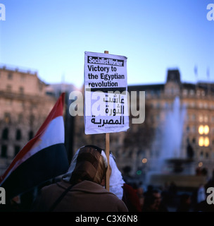 Donna egiziana (vista posteriore) sostenitrice donna che indossa il velo in piedi durante la dimostrazione a Trafalgar Square, tenendo un poster di lavoro socialista in lingua araba e inglese che sostiene la vittoria alla rivoluzione egiziana durante la rivolta della primavera araba in Egitto, Londra UK 2011 KATHY DEWITT Foto Stock